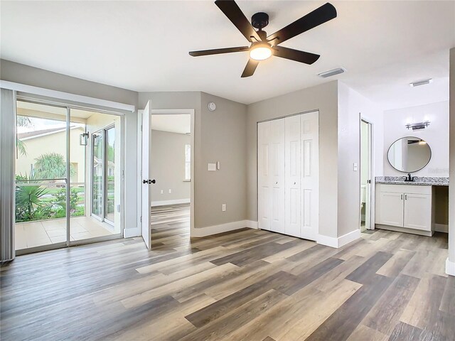 unfurnished bedroom featuring access to exterior, wood-type flooring, ceiling fan, ensuite bathroom, and sink