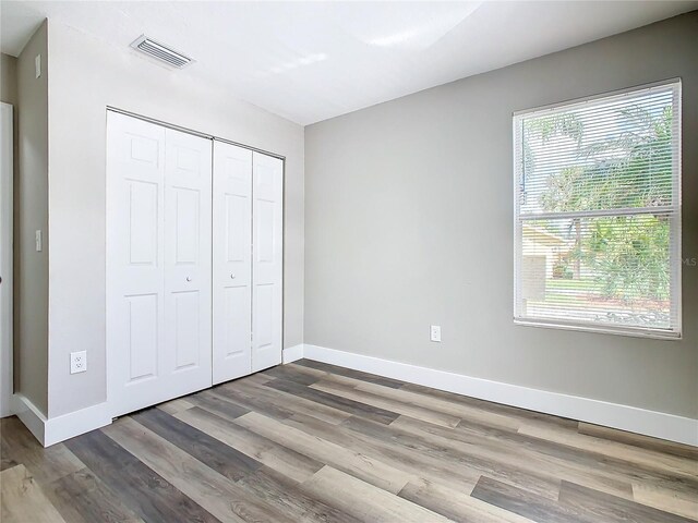 unfurnished bedroom with multiple windows, wood-type flooring, and a closet