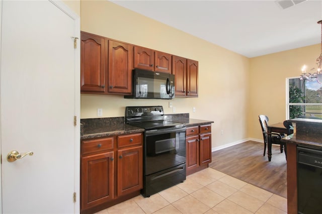 kitchen featuring light hardwood / wood-style floors, an inviting chandelier, dark stone counters, and black appliances