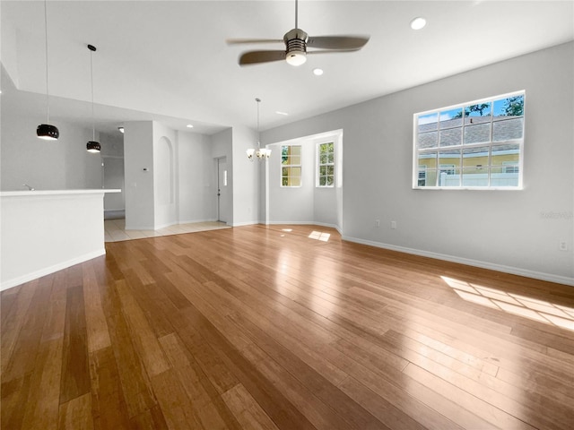 unfurnished living room with ceiling fan with notable chandelier and light hardwood / wood-style flooring