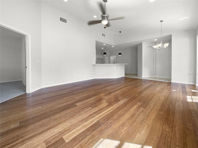 unfurnished living room with ceiling fan with notable chandelier, a high ceiling, and hardwood / wood-style floors