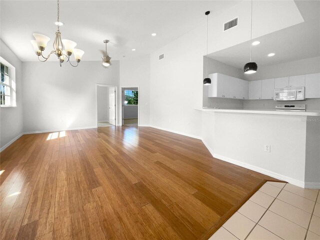 unfurnished living room with a notable chandelier, light wood-type flooring, and plenty of natural light