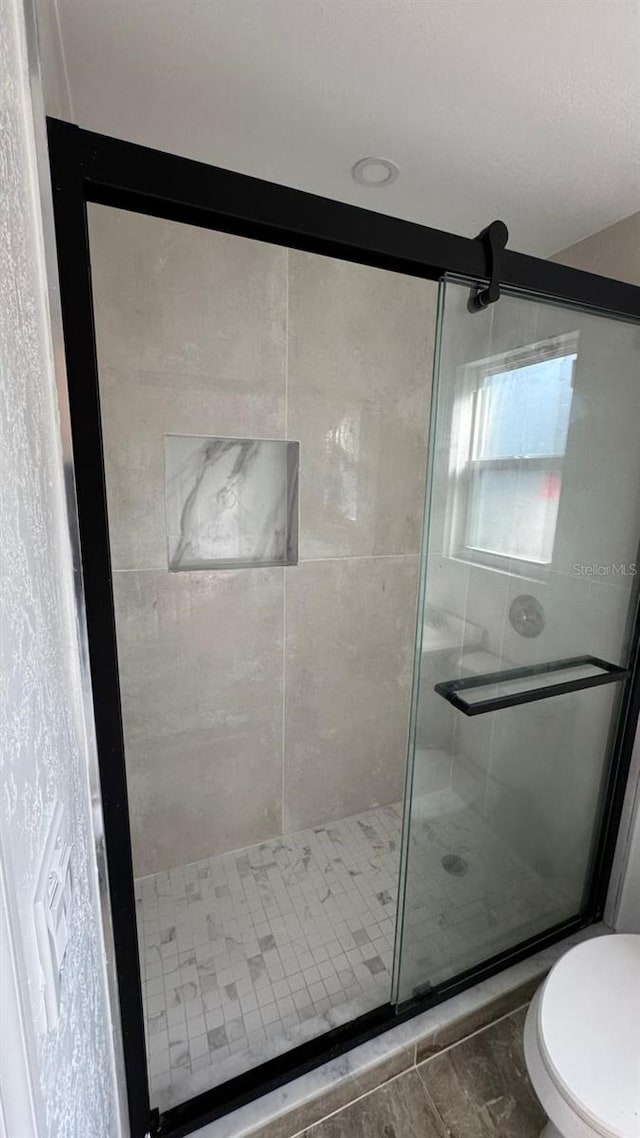 bathroom featuring a shower with door and toilet