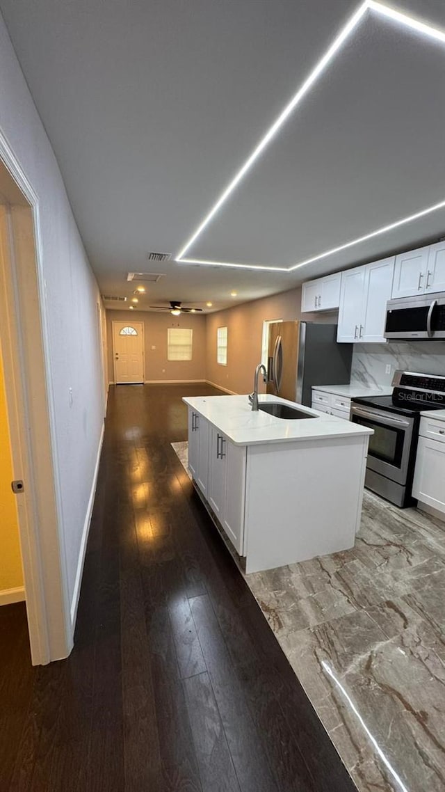 kitchen with tasteful backsplash, dark hardwood / wood-style flooring, appliances with stainless steel finishes, an island with sink, and white cabinetry