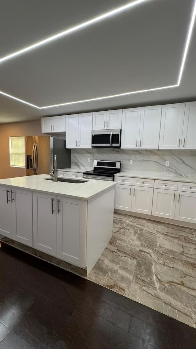 1517 S Campbell St, Perry, FL 32348 - kitchen featuring appliances with stainless steel finishes, white cabinets, an island with sink, light stone counters, and tasteful backsplash