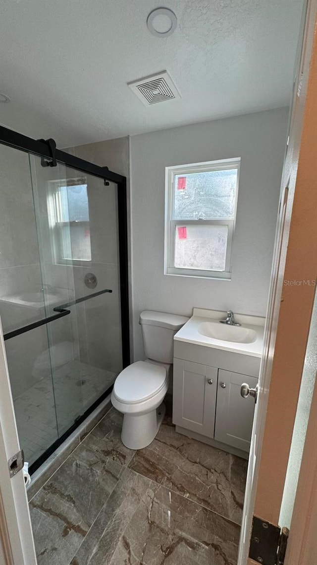 bathroom featuring a shower with door, vanity, a textured ceiling, and toilet