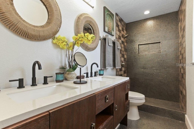 bathroom with tiled shower, vanity, a textured ceiling, toilet, and tile patterned floors