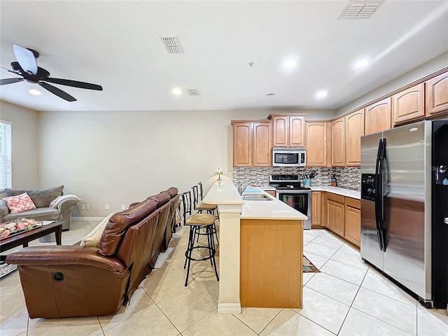 kitchen with appliances with stainless steel finishes, kitchen peninsula, a kitchen bar, ceiling fan, and sink