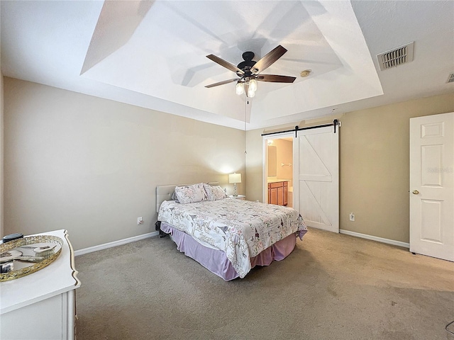 carpeted bedroom with a barn door, a tray ceiling, ceiling fan, and ensuite bathroom