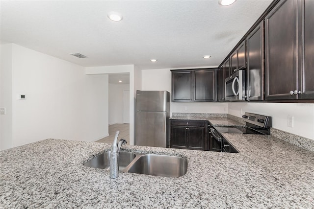 kitchen featuring appliances with stainless steel finishes, light stone countertops, a textured ceiling, dark brown cabinets, and sink