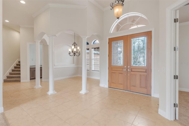 tiled foyer featuring ornamental molding, french doors, decorative columns, a notable chandelier, and a towering ceiling