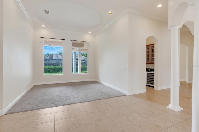 carpeted spare room with sink, wine cooler, crown molding, and ornate columns