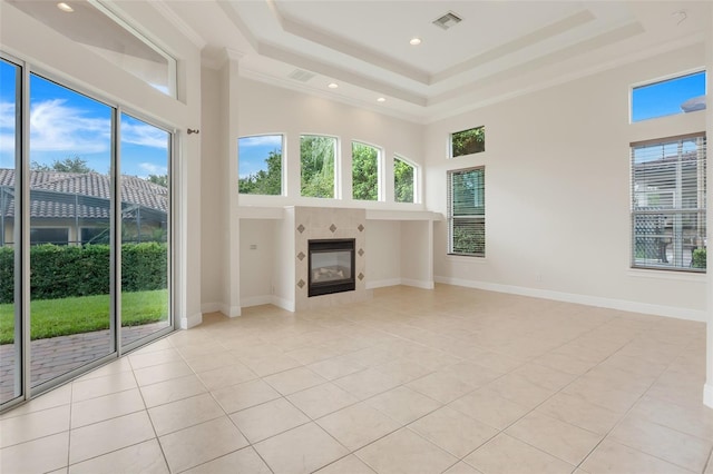 unfurnished living room with a tray ceiling, a towering ceiling, light tile patterned floors, and crown molding