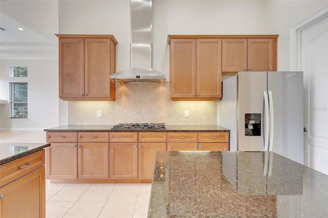 kitchen with appliances with stainless steel finishes, dark stone countertops, tasteful backsplash, light tile patterned floors, and wall chimney range hood