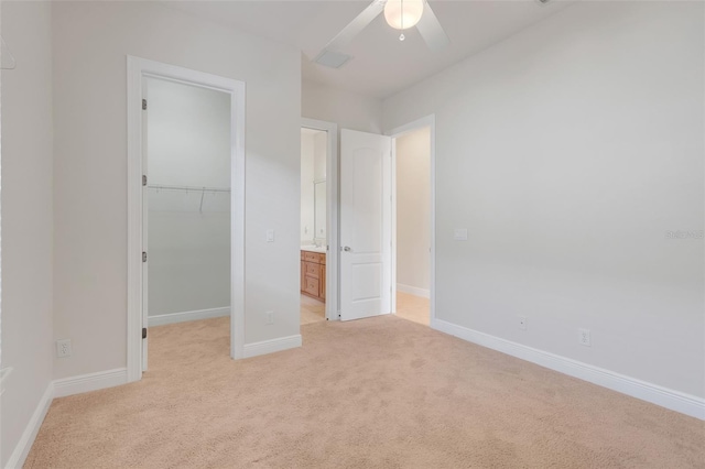 unfurnished bedroom featuring a walk in closet, ceiling fan, light colored carpet, and a closet