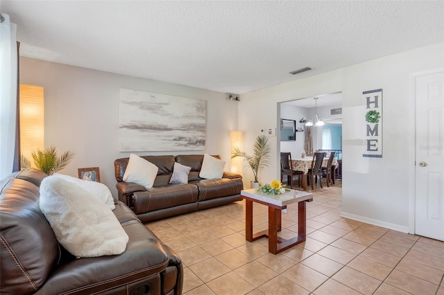 living area featuring light tile patterned floors, baseboards, visible vents, a textured ceiling, and a chandelier