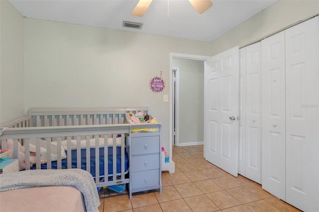 tiled bedroom with ceiling fan, a closet, a textured ceiling, and a nursery area