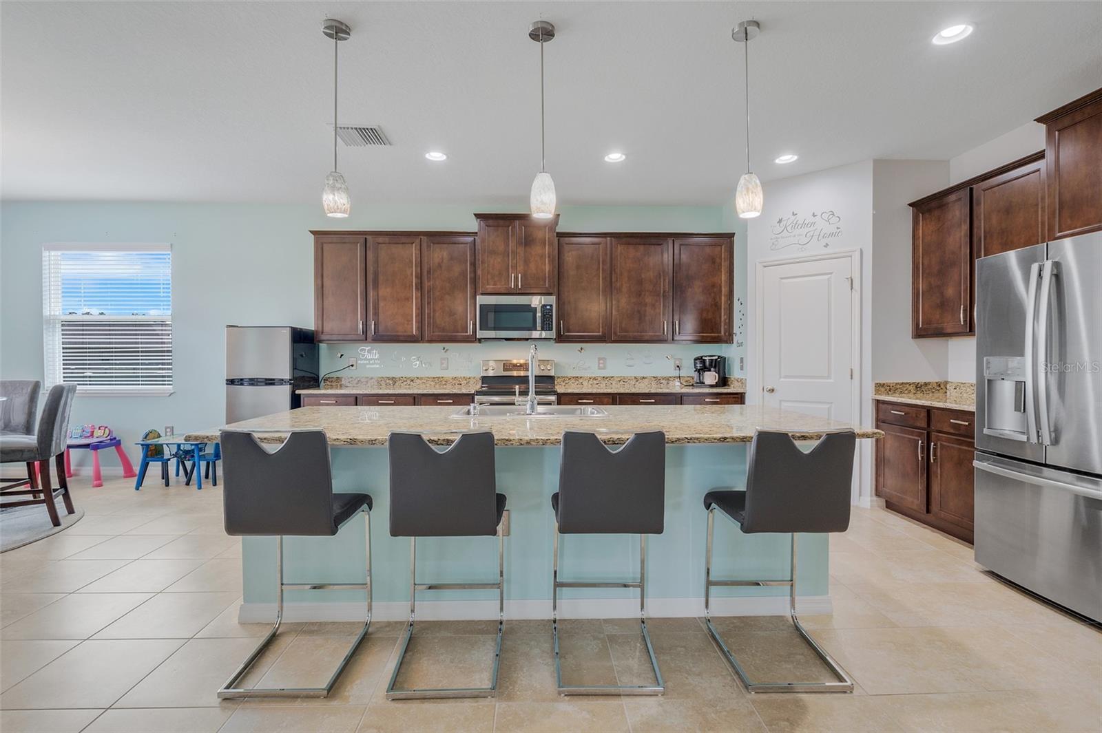 kitchen with appliances with stainless steel finishes, hanging light fixtures, an island with sink, and light stone counters