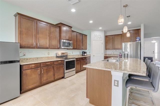 kitchen with light stone counters, sink, hanging light fixtures, a center island with sink, and appliances with stainless steel finishes