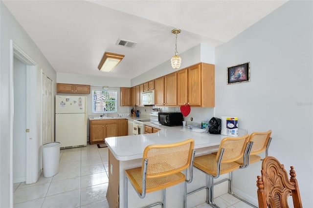 kitchen featuring pendant lighting, light tile patterned floors, kitchen peninsula, white appliances, and a kitchen bar