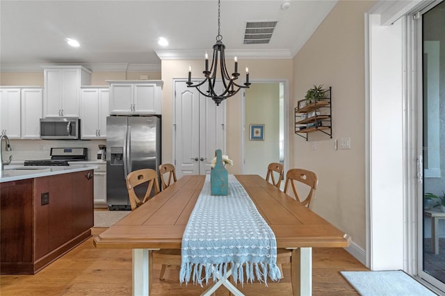 dining room featuring a notable chandelier, light wood-type flooring, ornamental molding, and sink