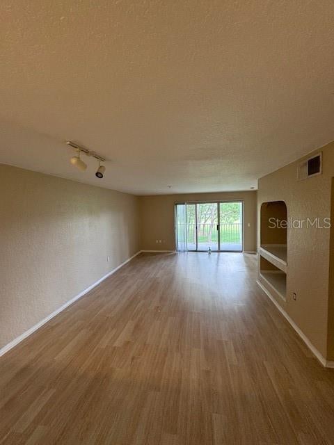 empty room with a textured ceiling, hardwood / wood-style floors, and track lighting