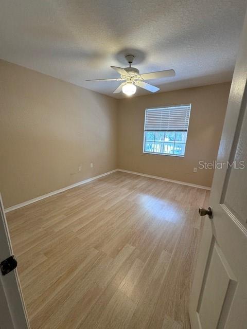 empty room with a textured ceiling, ceiling fan, and light hardwood / wood-style flooring