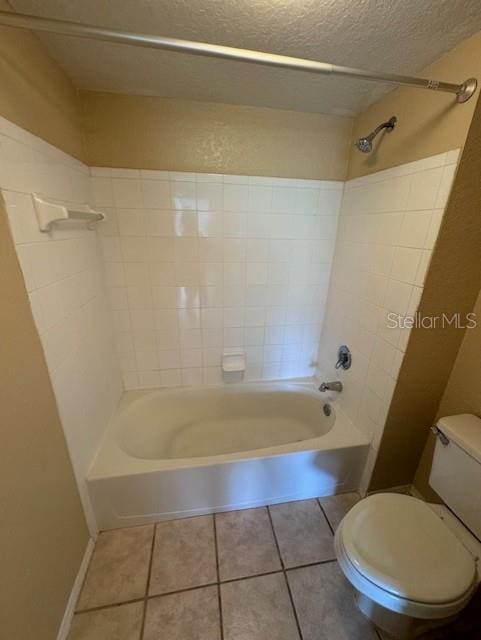 bathroom featuring a textured ceiling, tiled shower / bath combo, toilet, and tile patterned floors