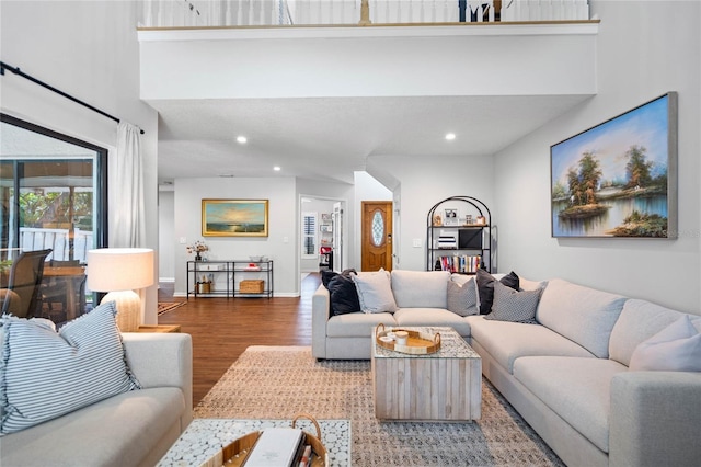 living area with baseboards, a high ceiling, wood finished floors, and recessed lighting
