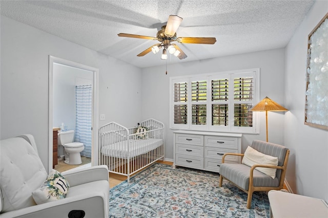 bedroom featuring a ceiling fan, a crib, ensuite bath, and a textured ceiling
