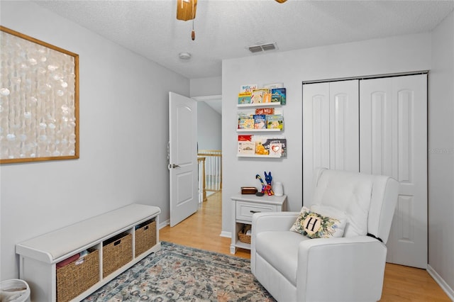 living area featuring baseboards, a textured ceiling, visible vents, and light wood-type flooring