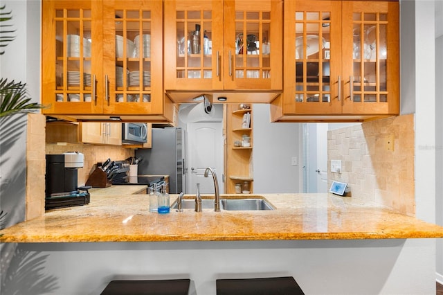kitchen with decorative backsplash, a peninsula, appliances with stainless steel finishes, glass insert cabinets, and a sink