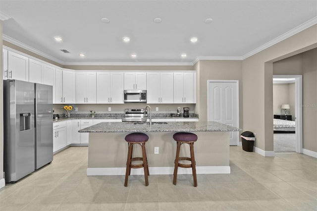 kitchen featuring light stone counters, a center island with sink, appliances with stainless steel finishes, and white cabinetry