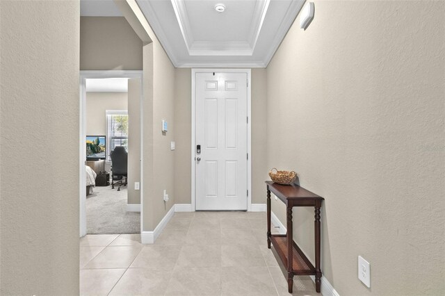 foyer entrance with crown molding, a tray ceiling, and light tile patterned floors