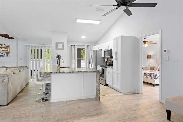 kitchen featuring white cabinets, appliances with stainless steel finishes, light stone countertops, and a breakfast bar