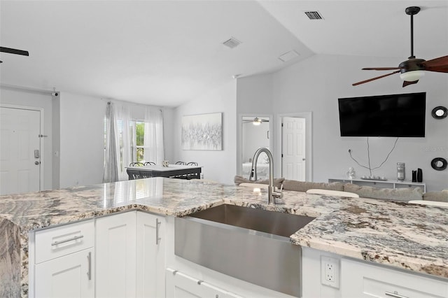 kitchen featuring lofted ceiling, sink, light stone counters, and white cabinets