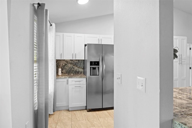 kitchen featuring white cabinets, vaulted ceiling, light stone counters, and stainless steel fridge