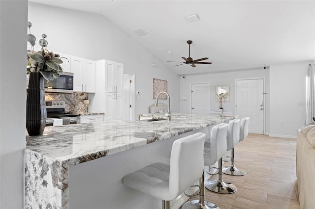 kitchen with a kitchen breakfast bar, white cabinetry, stainless steel appliances, lofted ceiling, and sink