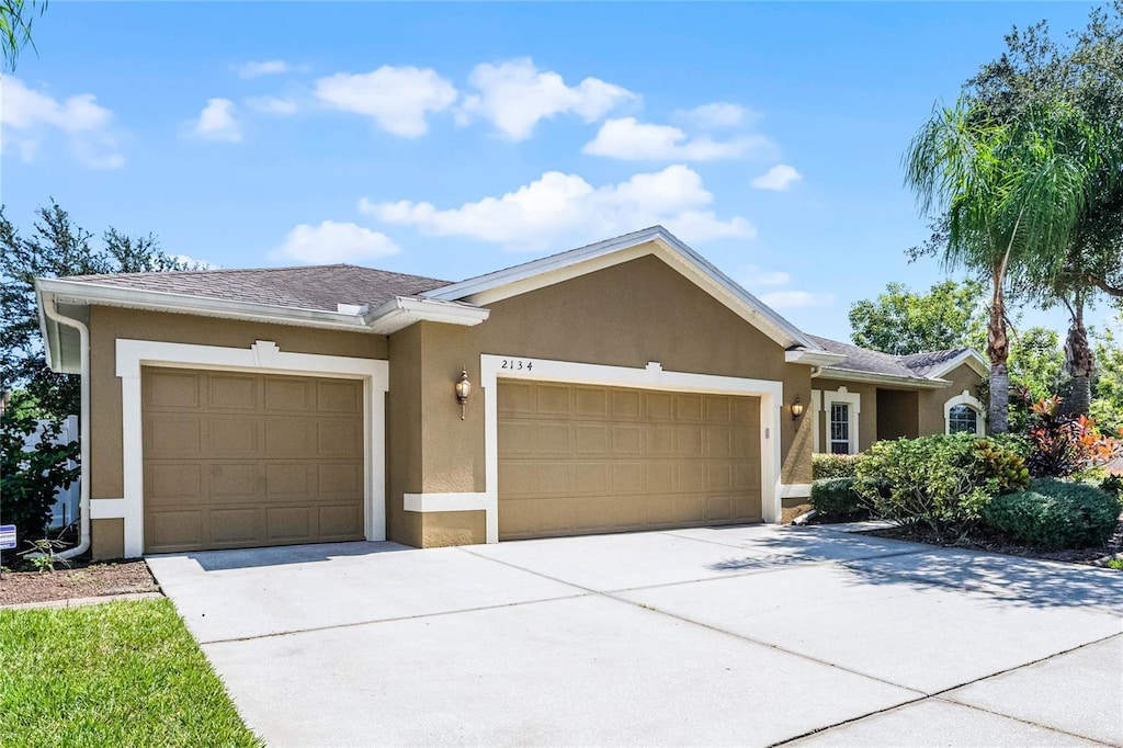 ranch-style home featuring concrete driveway, a shingled roof, an attached garage, and stucco siding