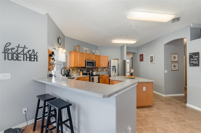 kitchen featuring kitchen peninsula, tasteful backsplash, a textured ceiling, stainless steel appliances, and a breakfast bar area