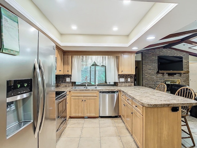 kitchen featuring a breakfast bar area, kitchen peninsula, sink, a brick fireplace, and appliances with stainless steel finishes