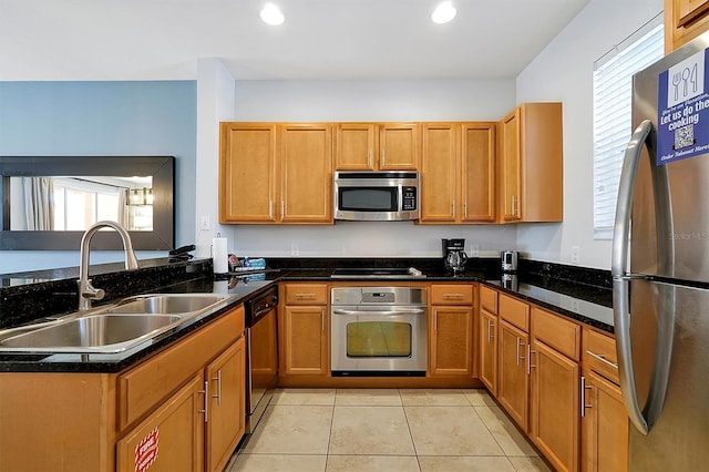 kitchen featuring dark stone countertops, light tile patterned flooring, kitchen peninsula, stainless steel appliances, and sink