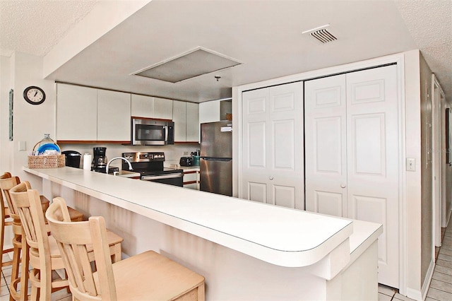 kitchen featuring stainless steel appliances, a peninsula, light countertops, and a kitchen breakfast bar