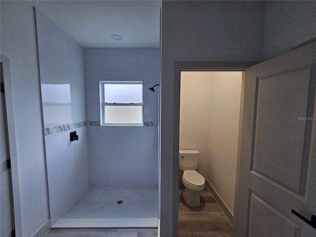 bathroom featuring a tile shower, toilet, and wood-type flooring