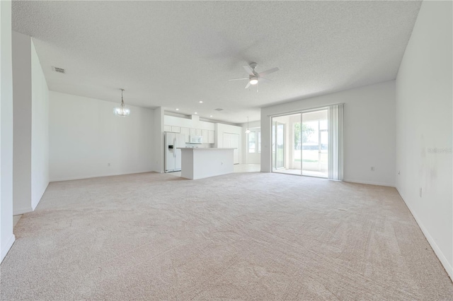 unfurnished living room with a textured ceiling, ceiling fan with notable chandelier, and light carpet