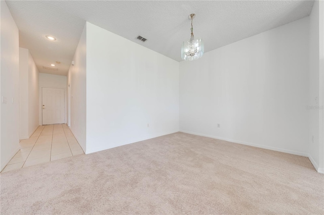 carpeted spare room with a textured ceiling and a chandelier