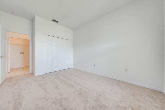 unfurnished bedroom featuring a textured ceiling, light carpet, and a closet