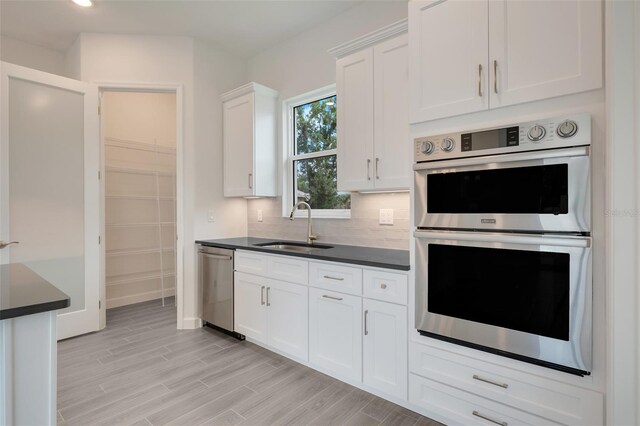 kitchen featuring sink, tasteful backsplash, white cabinetry, stainless steel appliances, and light hardwood / wood-style floors