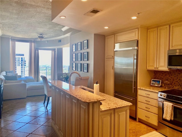 kitchen featuring an island with sink, light stone counters, tasteful backsplash, stainless steel appliances, and sink