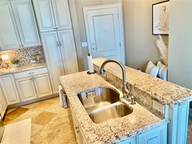 kitchen with a kitchen island with sink, sink, light stone counters, and tasteful backsplash